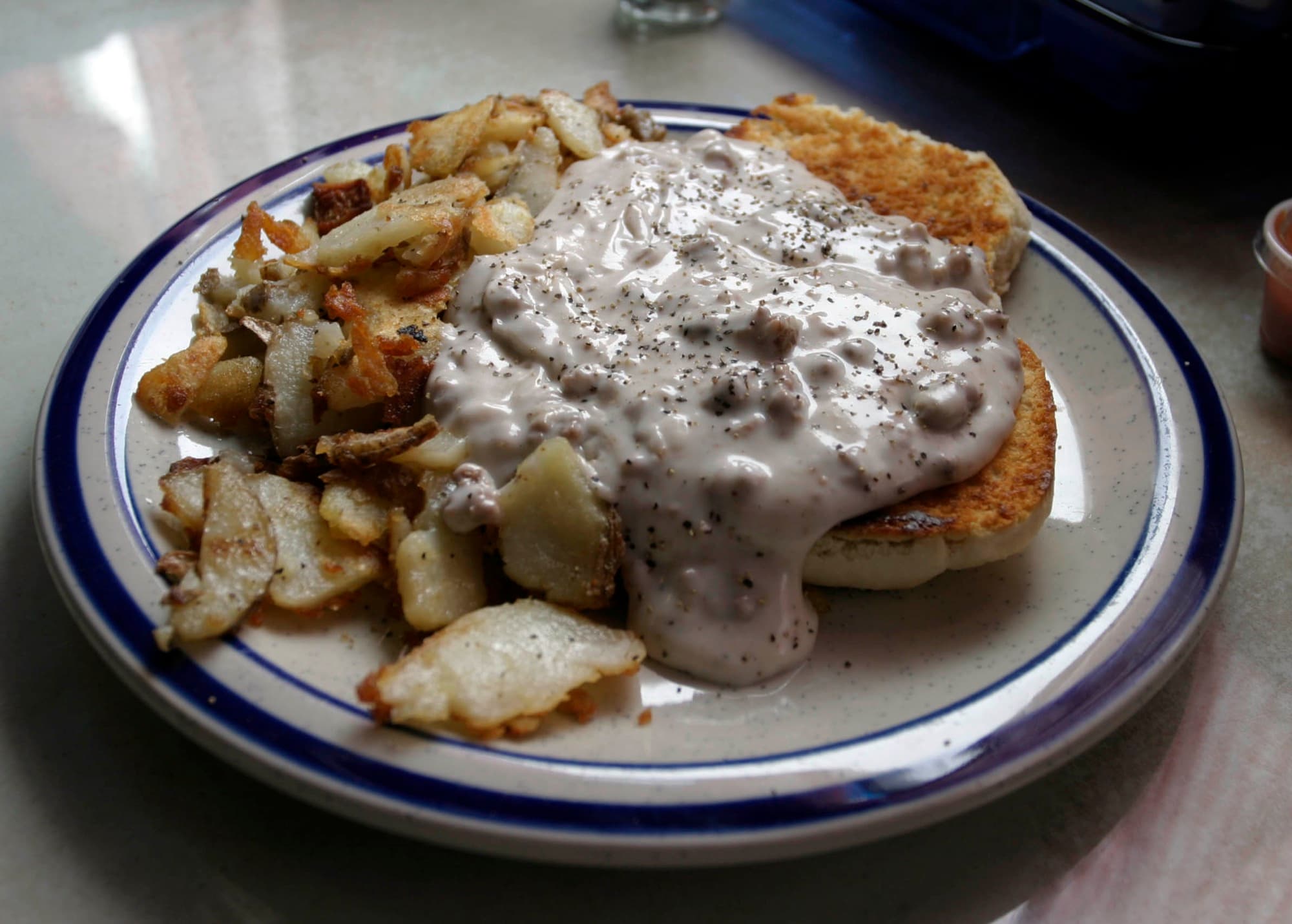 A plate of biscuits and gravy with a side of home fries.