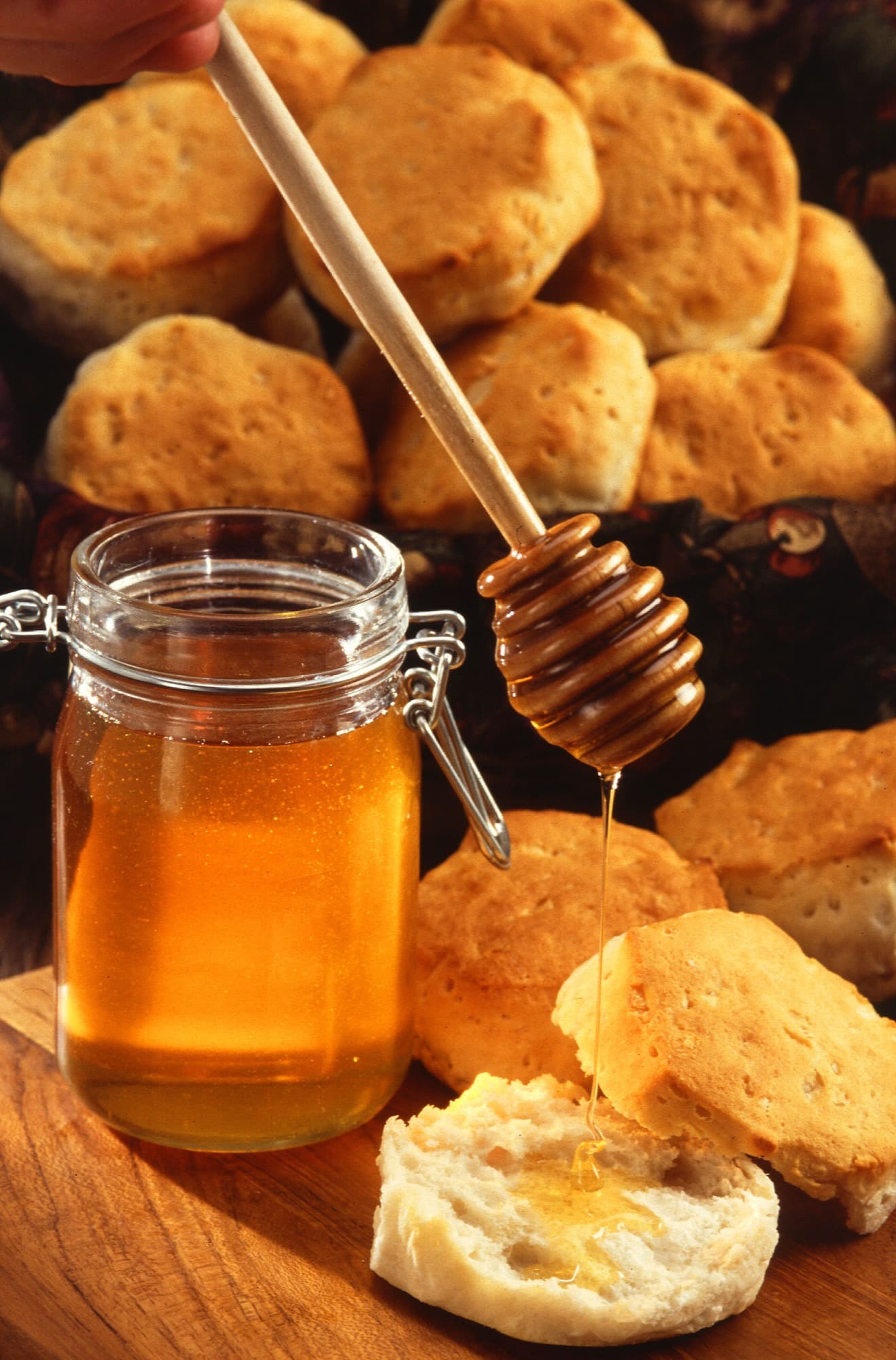 A jar of honey with a wooden honey dipper, next to a slice of bread.