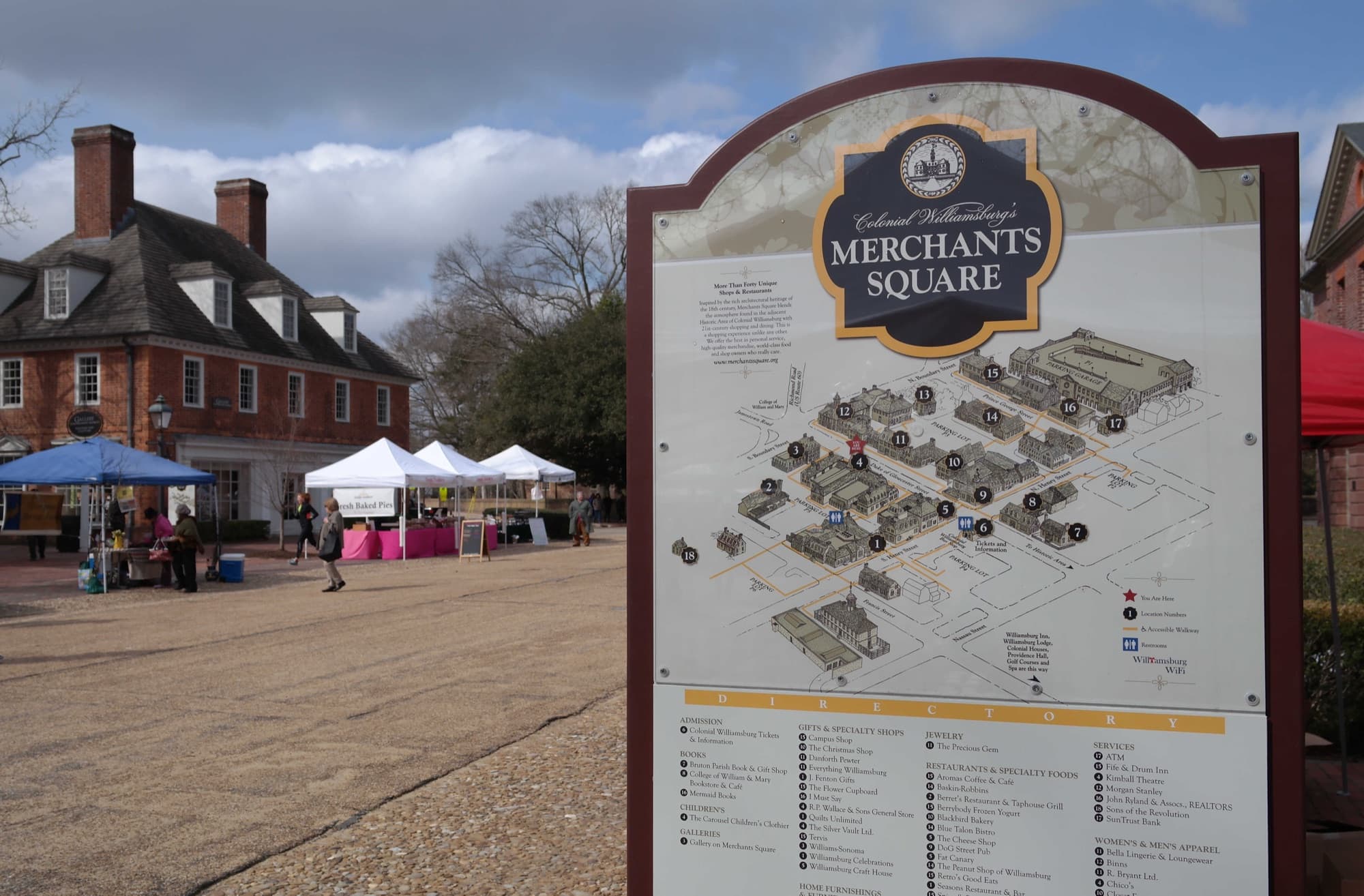 A row of vendor tents at an outdoor farmers market, with historic brick buildings in the background.